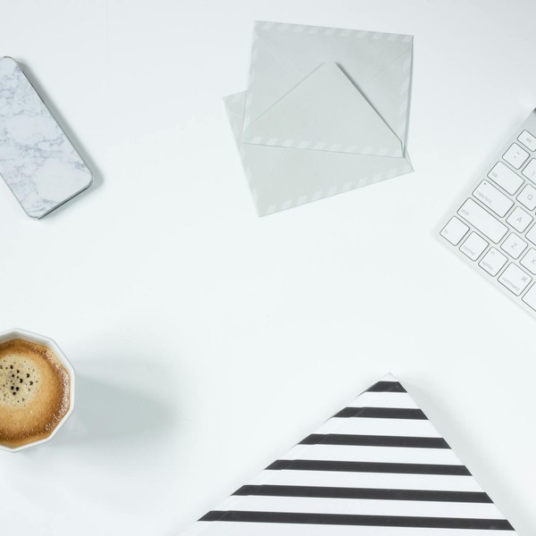 Clean minimalist workspace featuring coffee, keyboard, phone, and envelopes on a white desk.